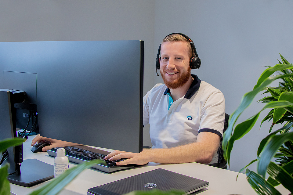 Person mit Headset sitzt am Schreibtisch vor einem Computer